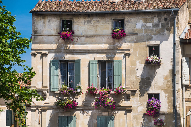 An old tile roofed hotel with light blue shutters and flowers hanging